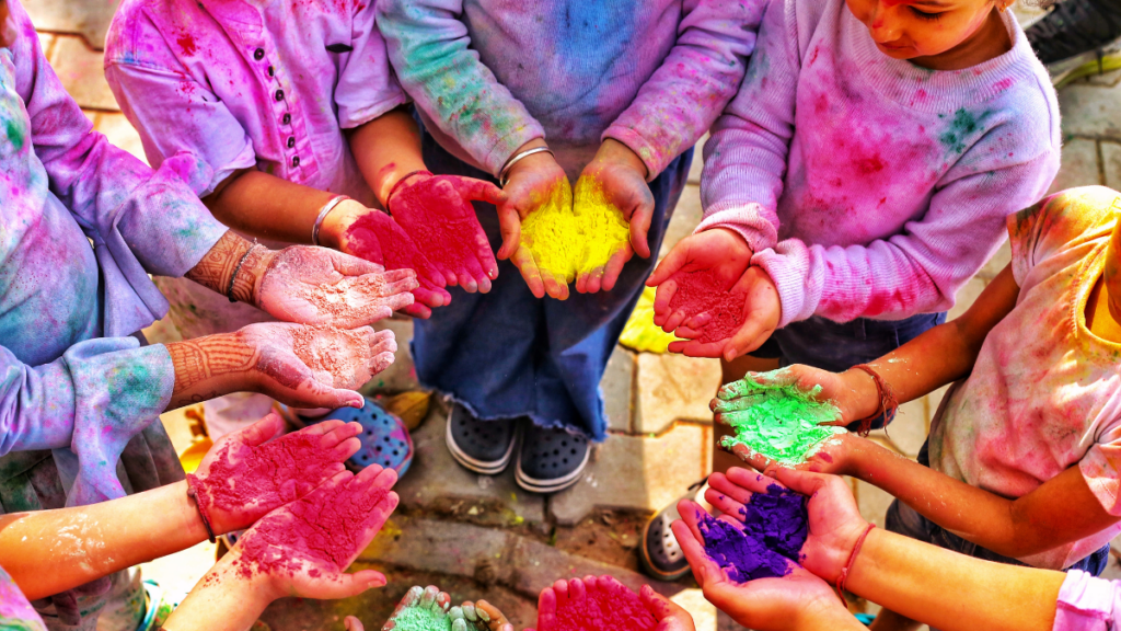 5 Vibrant Books about Holi, the Hindu Festival of Colors 1 Read books about Holi! This image shows kids celebrating Holi in a circle holding gulal or colored-powder in their hands. Their white clothes are stained with bright colors.